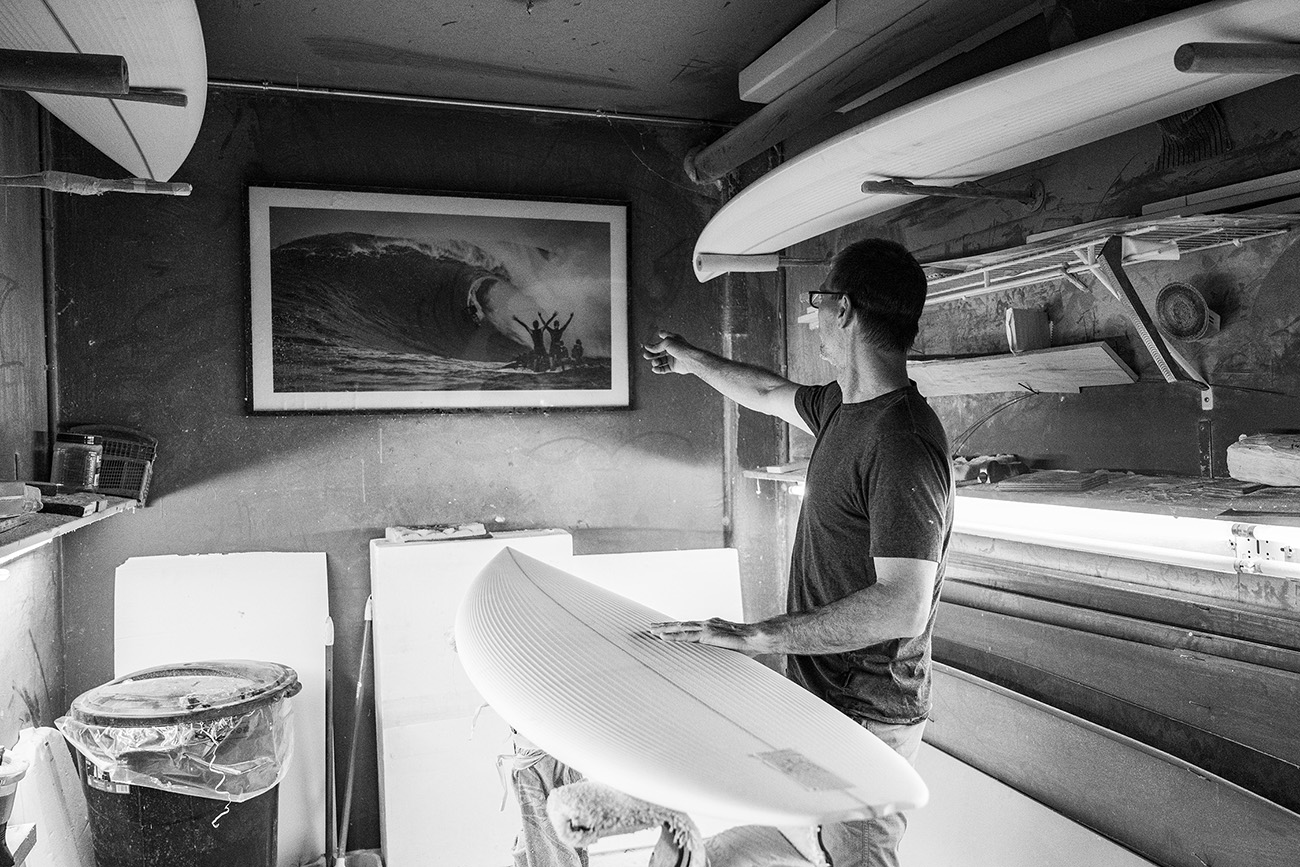 Sean in his shaping bay, pointing to a photograph of a breaking wave