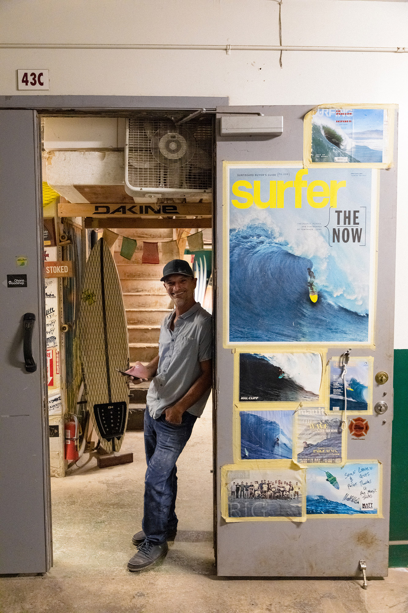 Sean standing in his Maui workshop doorway beside surf magazine covers